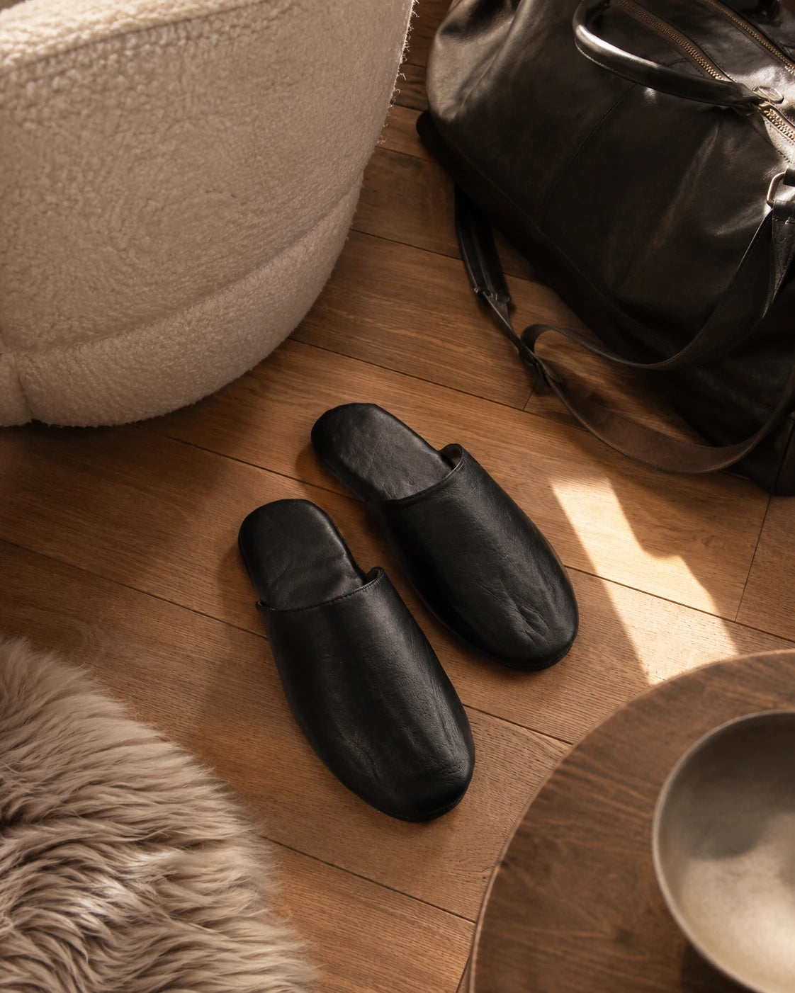 Black lambskin travel slippers styled beside an open carry-on suitcase