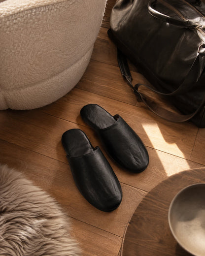 Black lambskin travel slippers styled beside an open carry-on suitcase