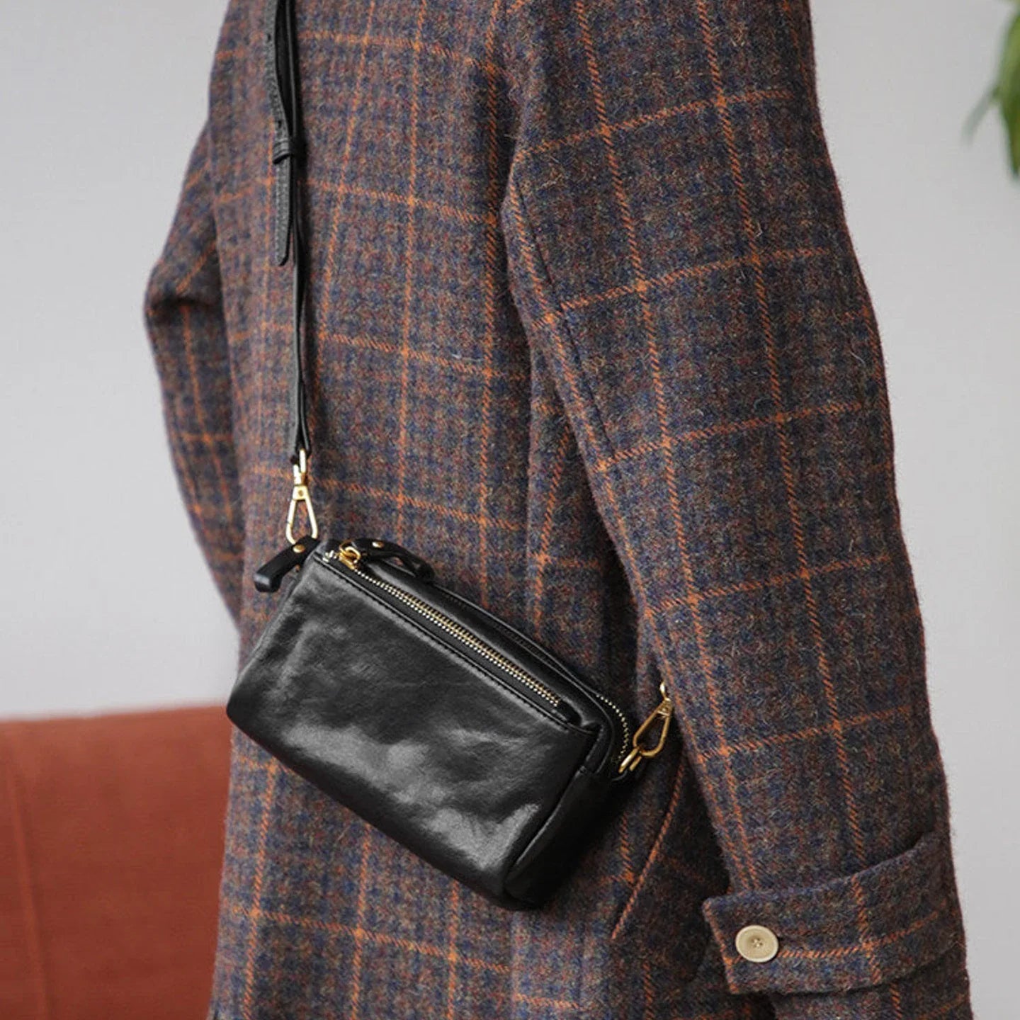 Side view of the black leather crossbody bag worn with a plaid coat