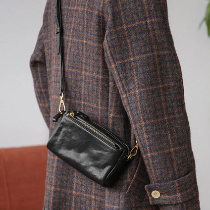 Side view of the black leather crossbody bag worn with a plaid coat