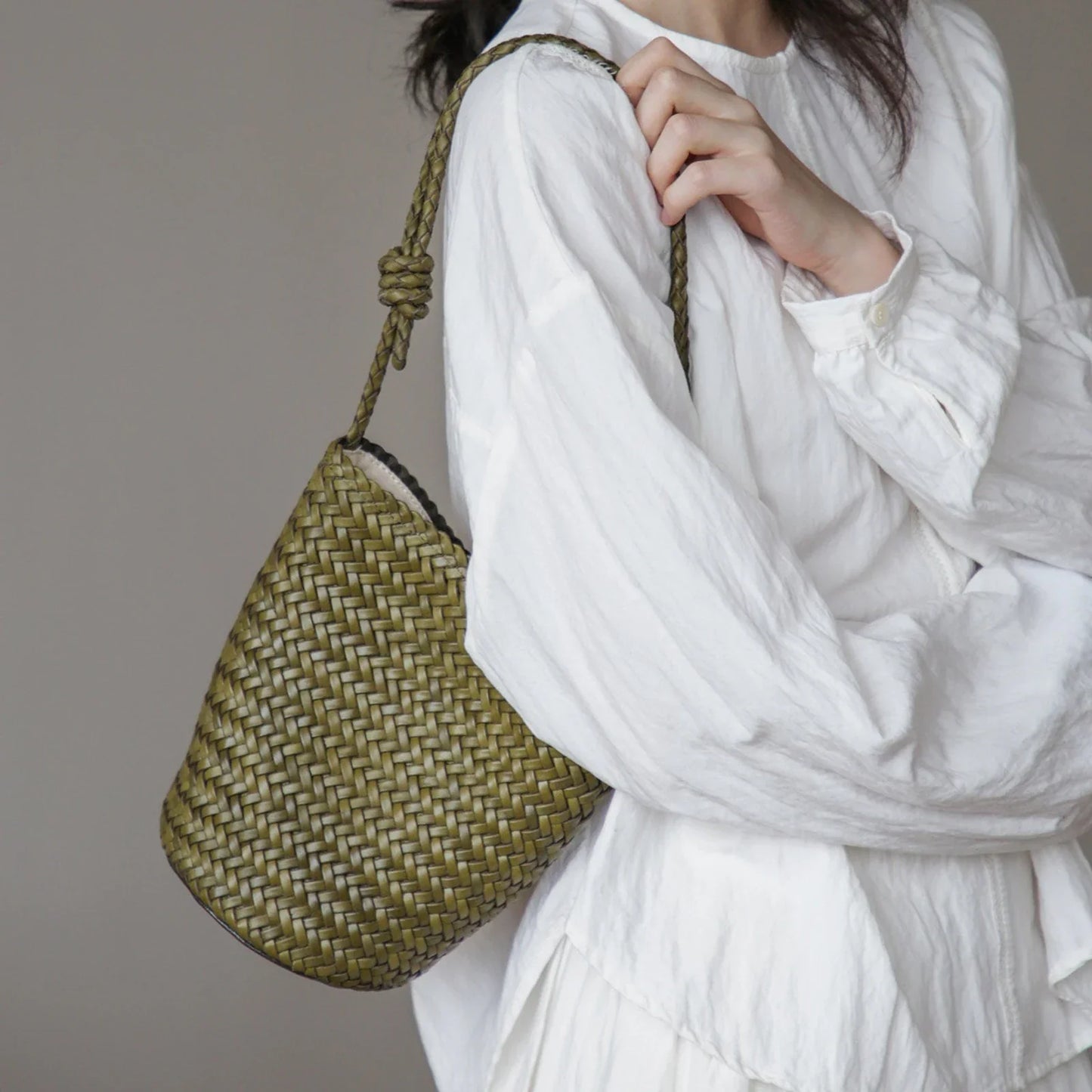 Olive green woven leather bucket bag showing the braided shoulder strap