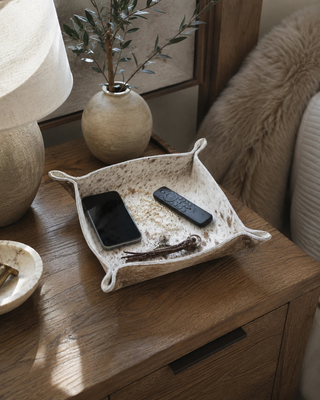 Speckled genuine cowhide valet tray holding a phone and remote controls on a wood side table