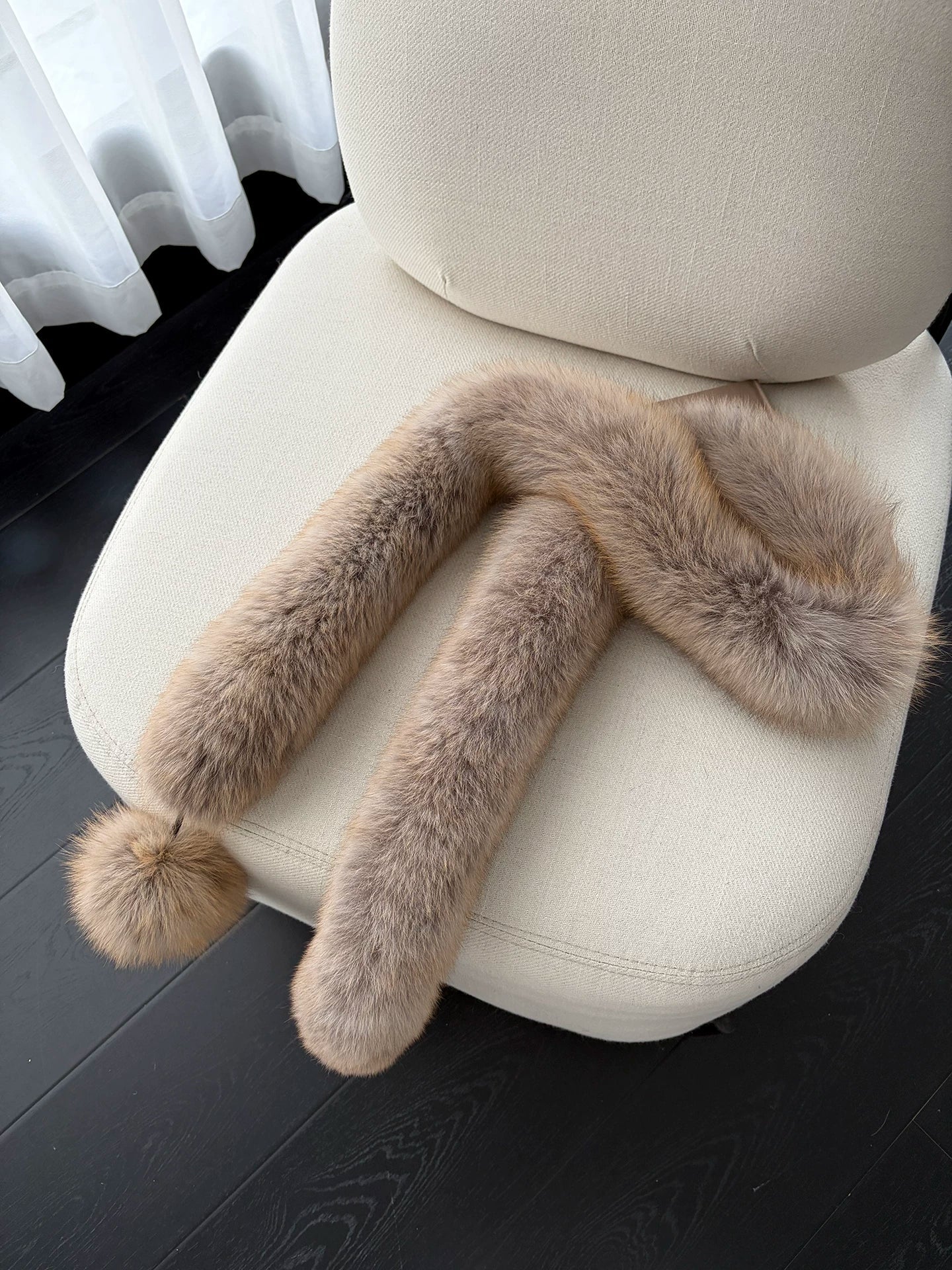 Golden Brown fox fur long scarf with pom-pom arranged on a cream chair