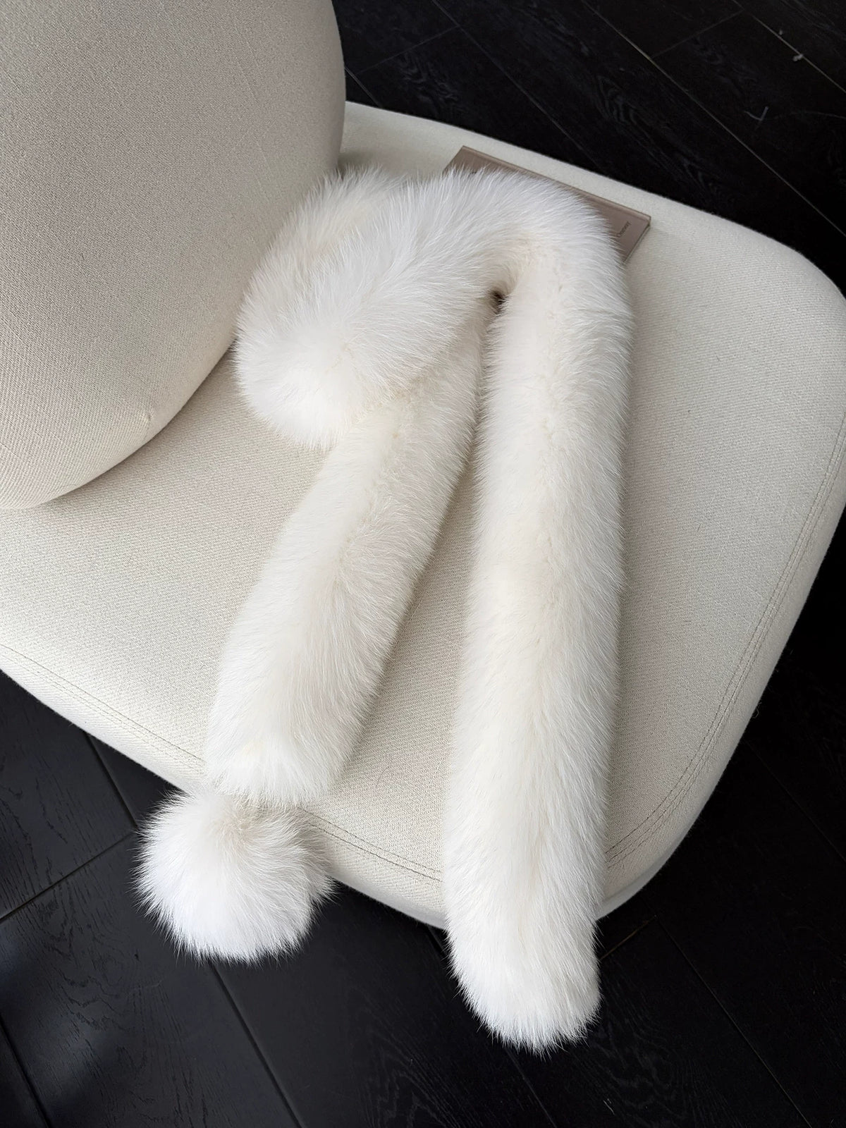 Cream Beige fox fur long scarf with pom-pom arranged on a cream chair