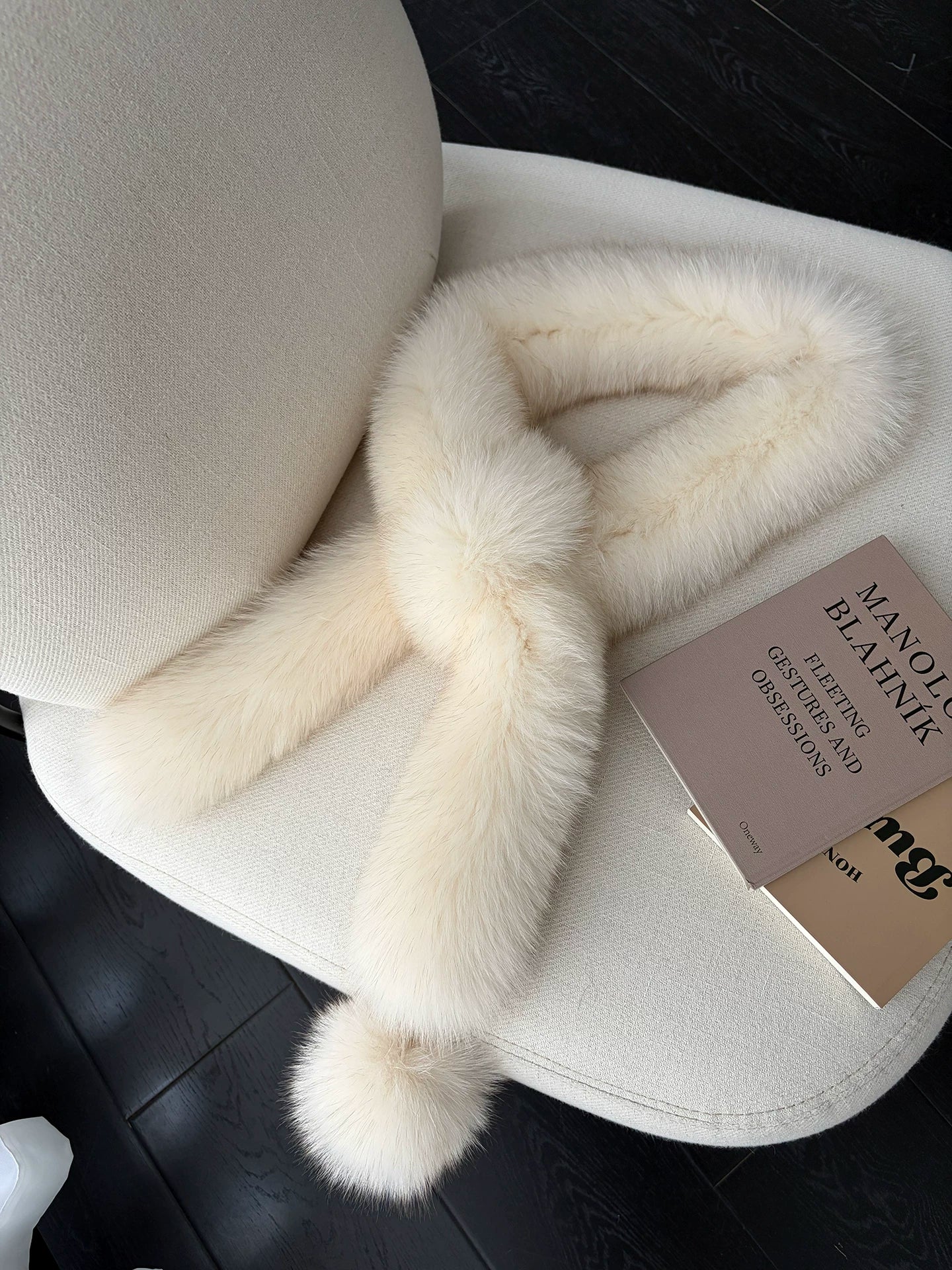 Apricot Beige fox fur long scarf with pom-pom arranged on a cream chair