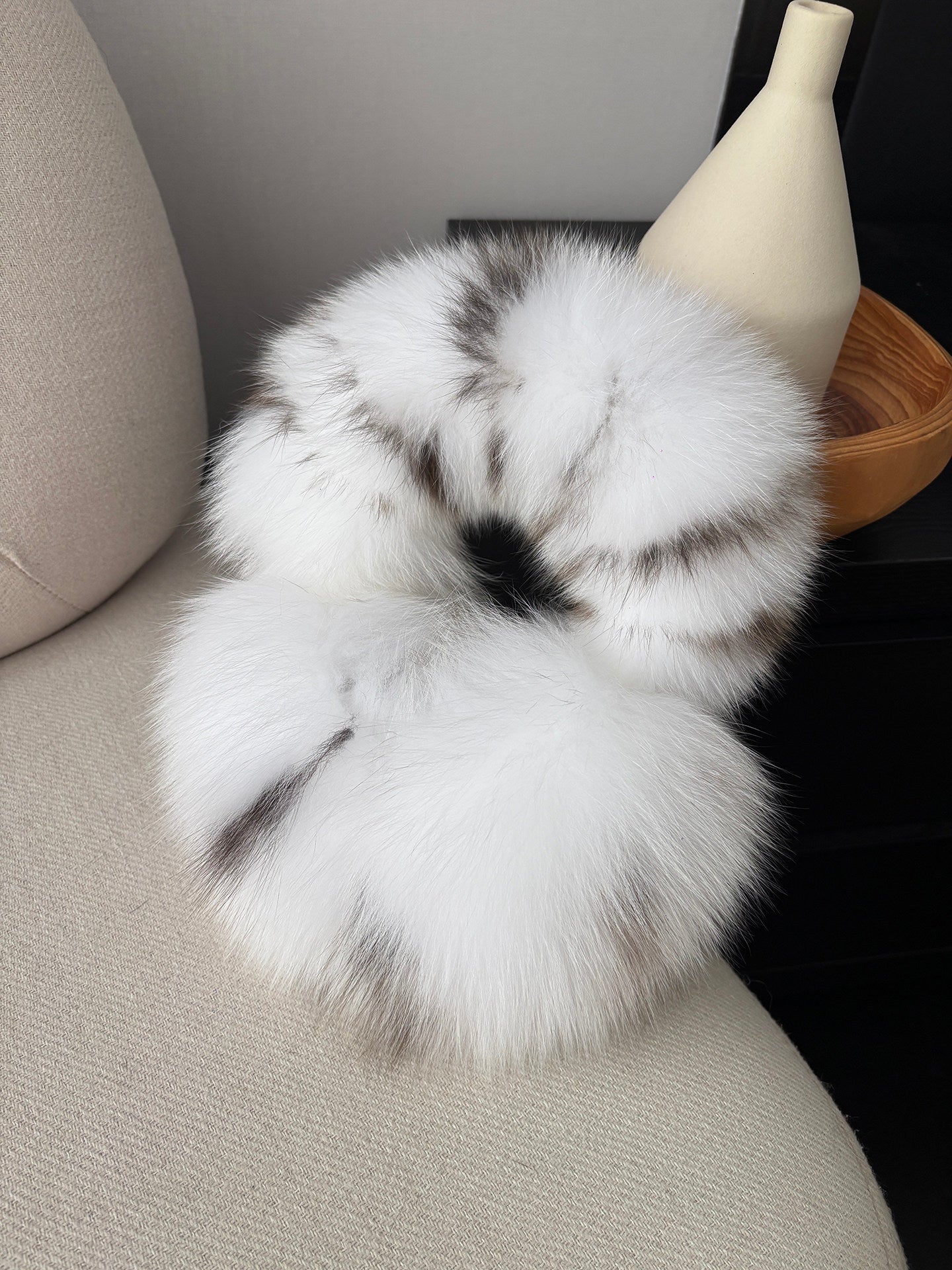 White Leopard fox fur earmuffs displayed on a neutral sofa