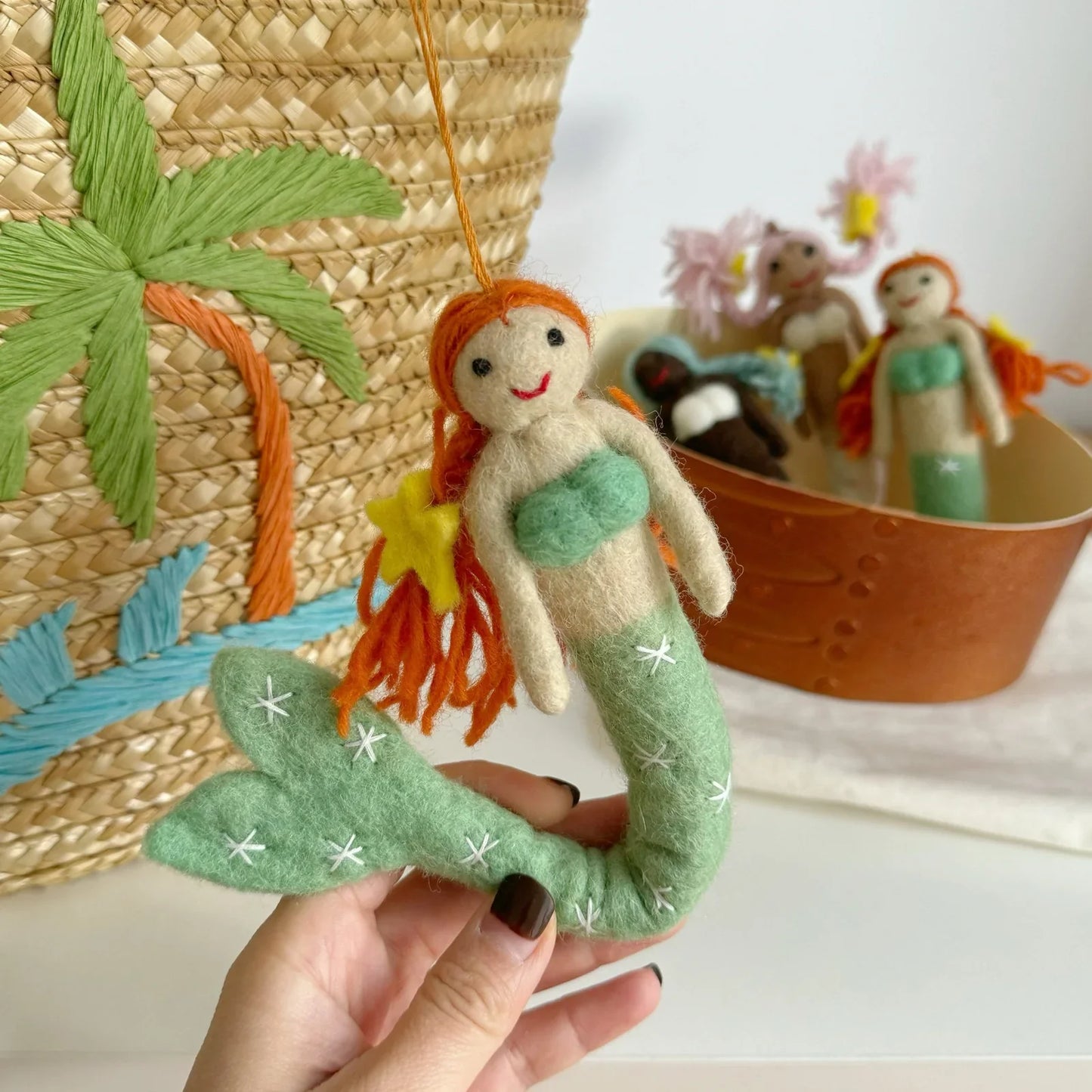 Green tail wool felt mermaid charm held beside a woven basket