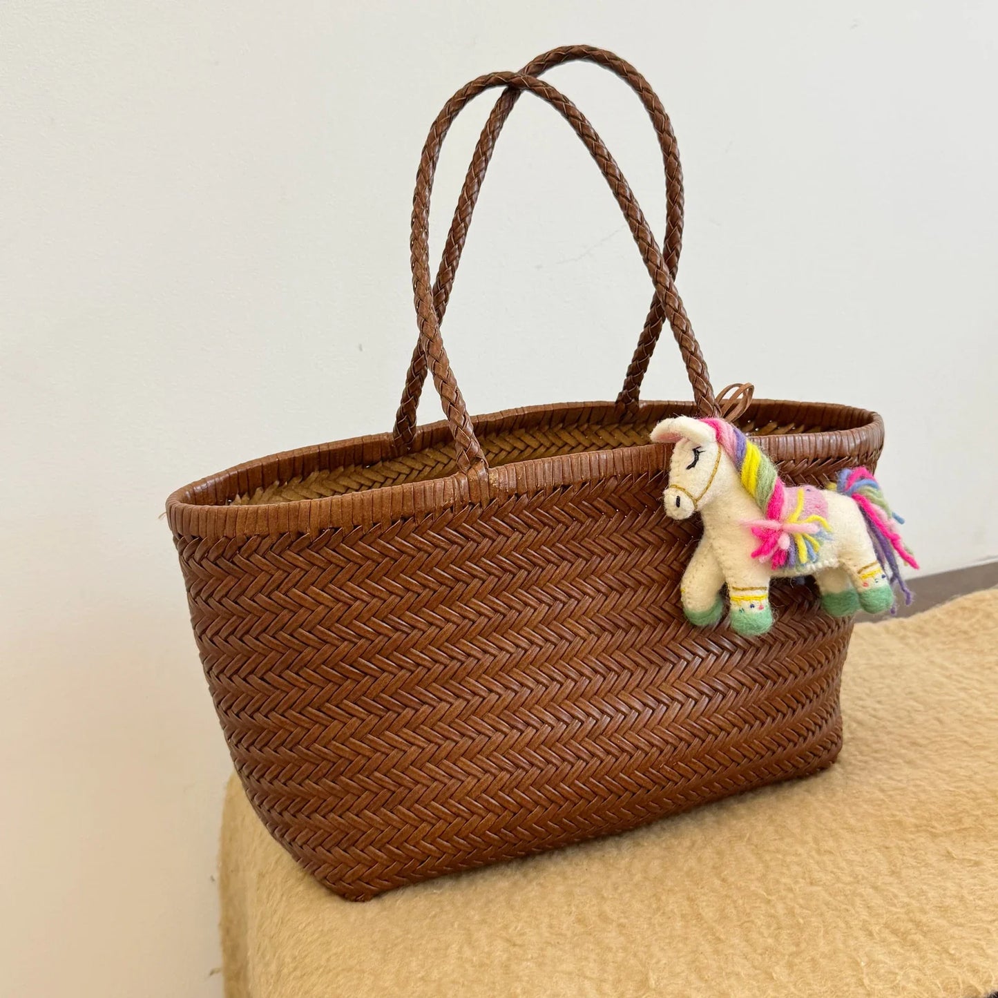Handmade multicolor wool felt horse charm styled on a woven handbag