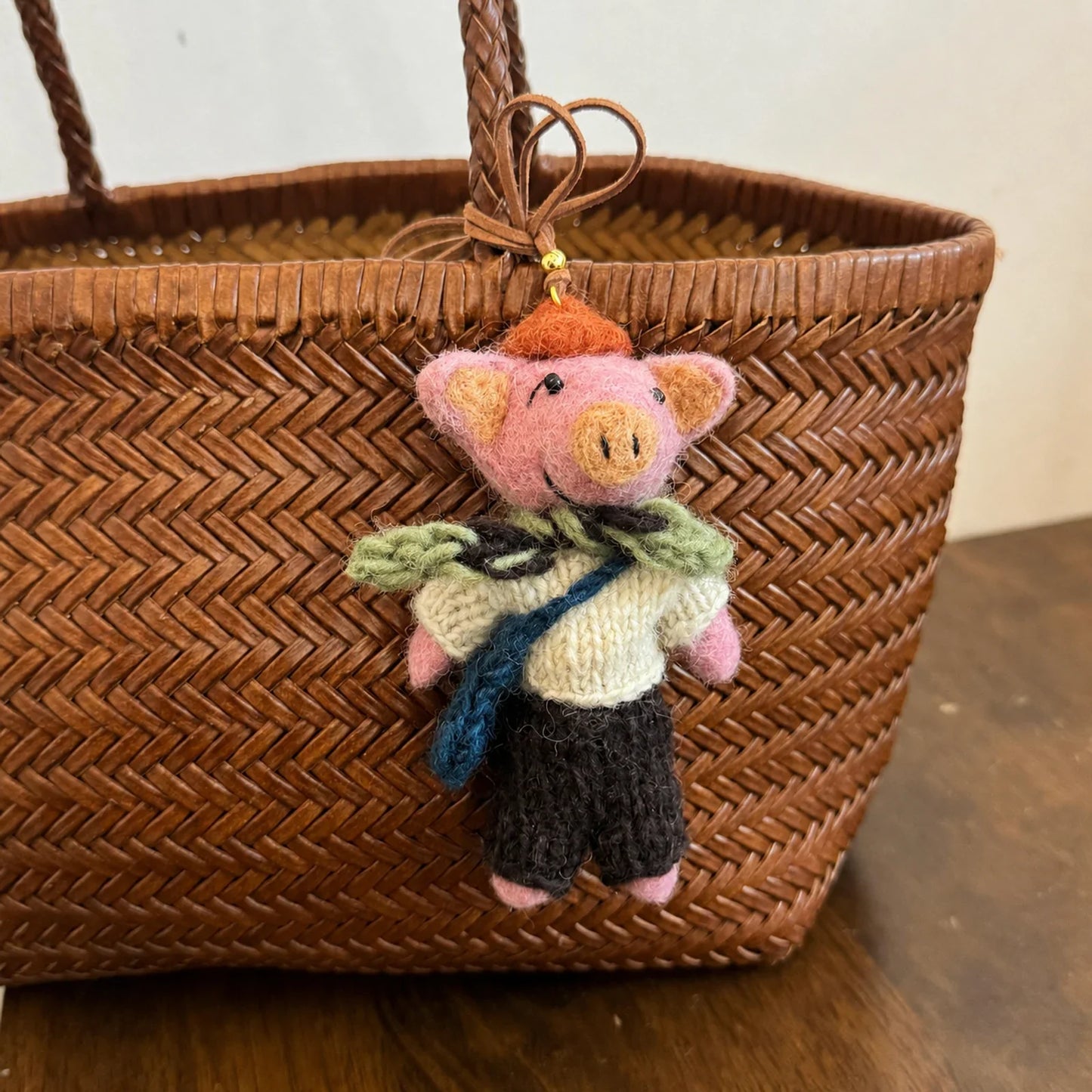 Handmade wool felt pig charm wearing a scarf on a woven bag