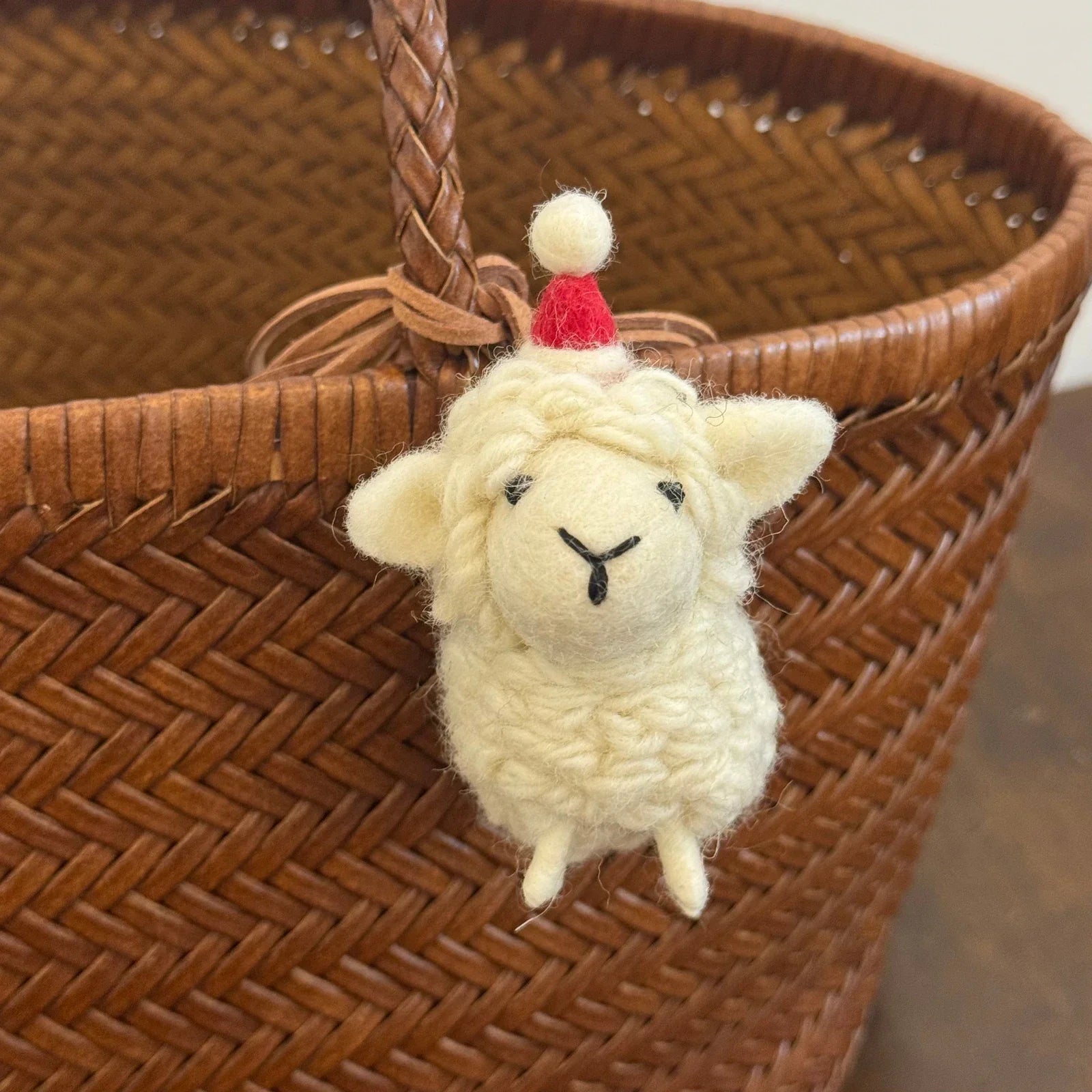 Cream wool felt sheep charm wearing a red pompom hat