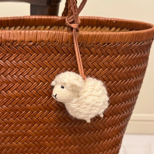 Handmade wool felt sheep bag charm displayed on a woven leather bag