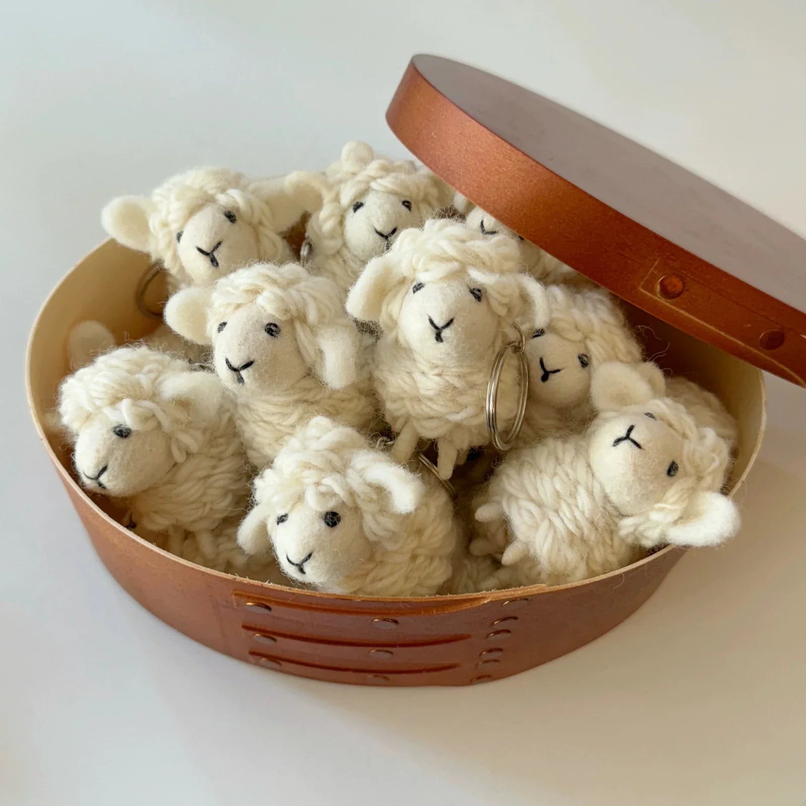 Collection of handmade wool felt sheep charms in a round leather box
