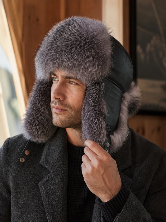 Man wearing a Silver Gray Fox fur trapper hat beside a cabin