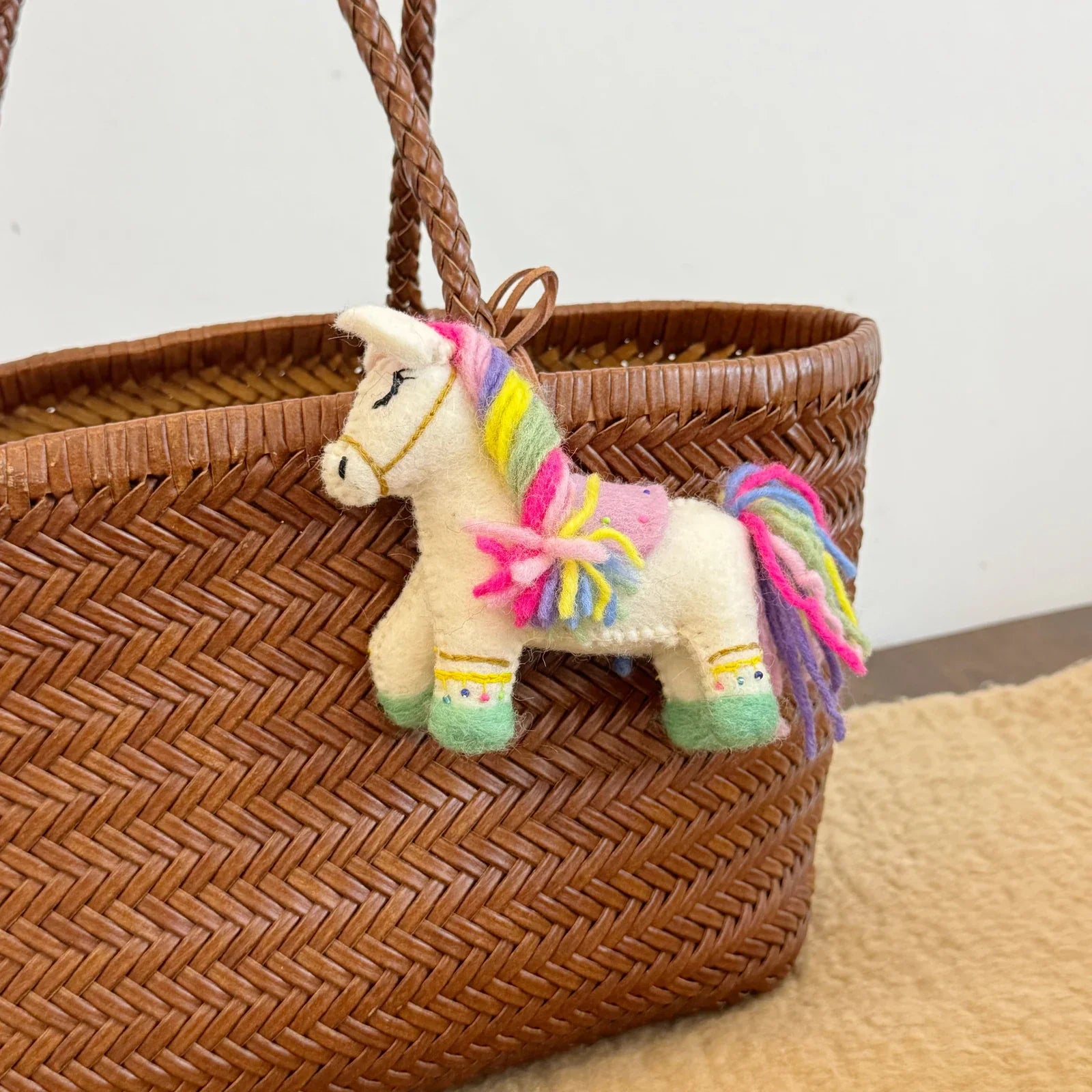 Multicolor handmade wool felt horse charm shown on a woven bag