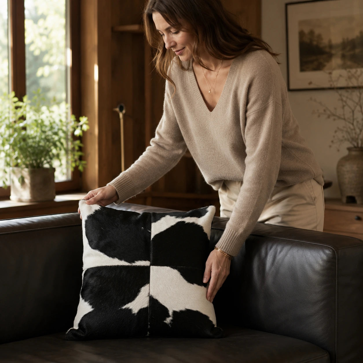 Woman arranging a black and white cowhide square pillow on a leather sofa