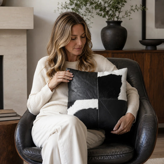 Woman over 35 holding an obsidian black leather and cowhide square pillow in a reading chair