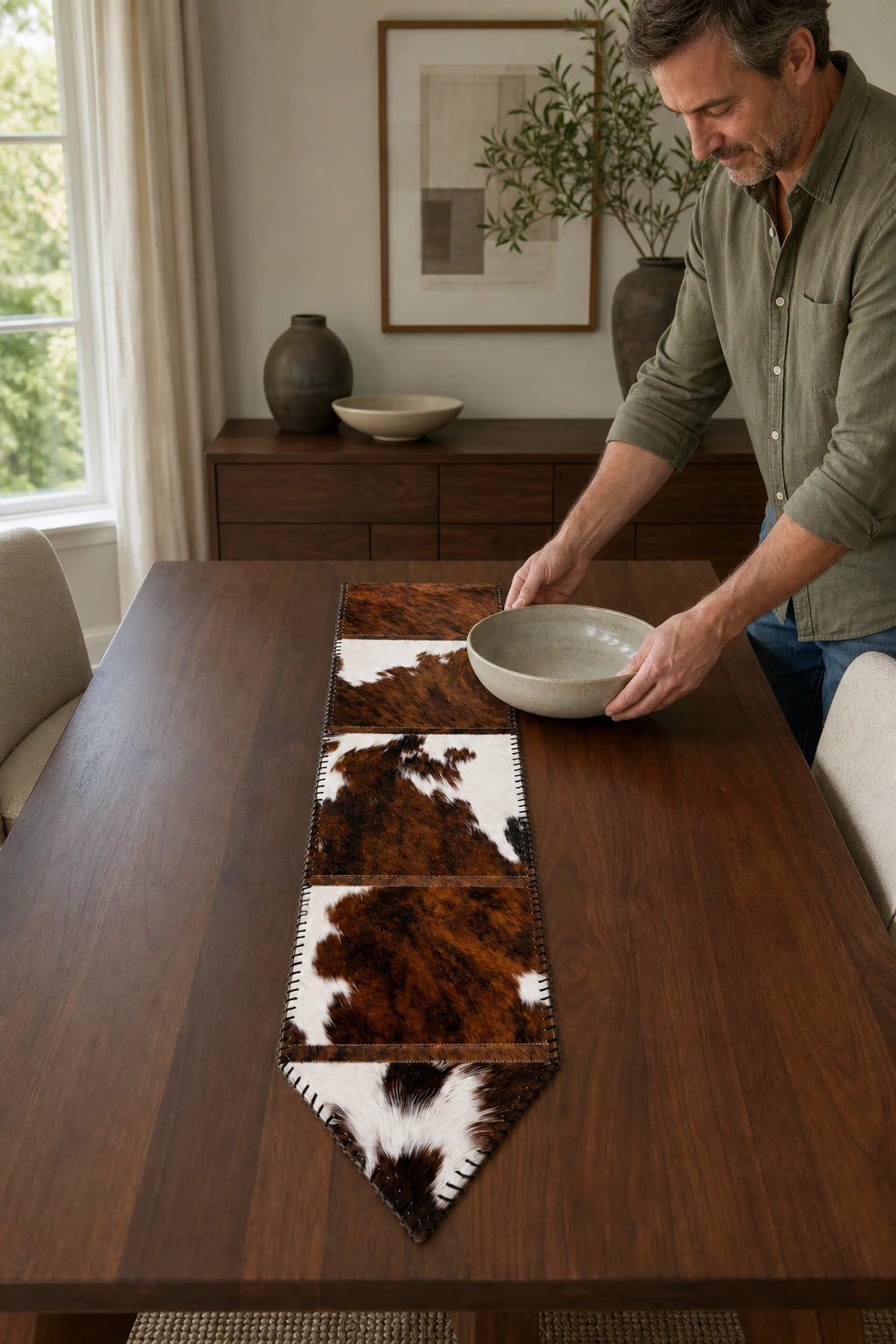 Capricornus Living Adult placing a bowl beside a Brown and White cowhide table runner in an American dining room