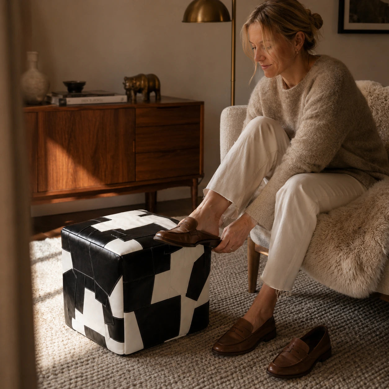 Woman over 35 using a black and ivory leather cube ottoman while changing shoes