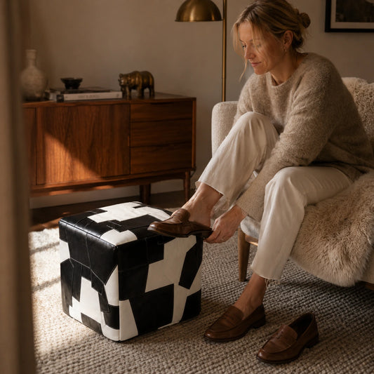 Woman over 35 using a black and ivory leather cube ottoman while changing shoes
