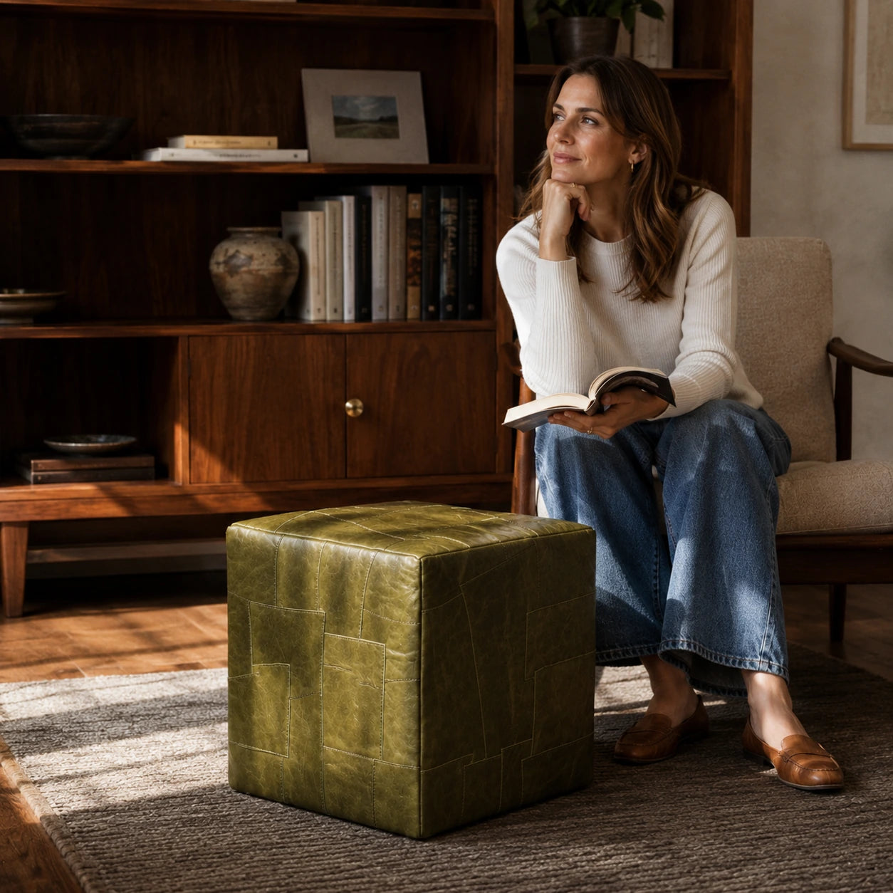 Woman over 35 using an olive green leather cube ottoman beside a reading chair