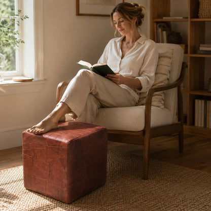 Woman over 35 using a brick brown leather cube ottoman as a footrest