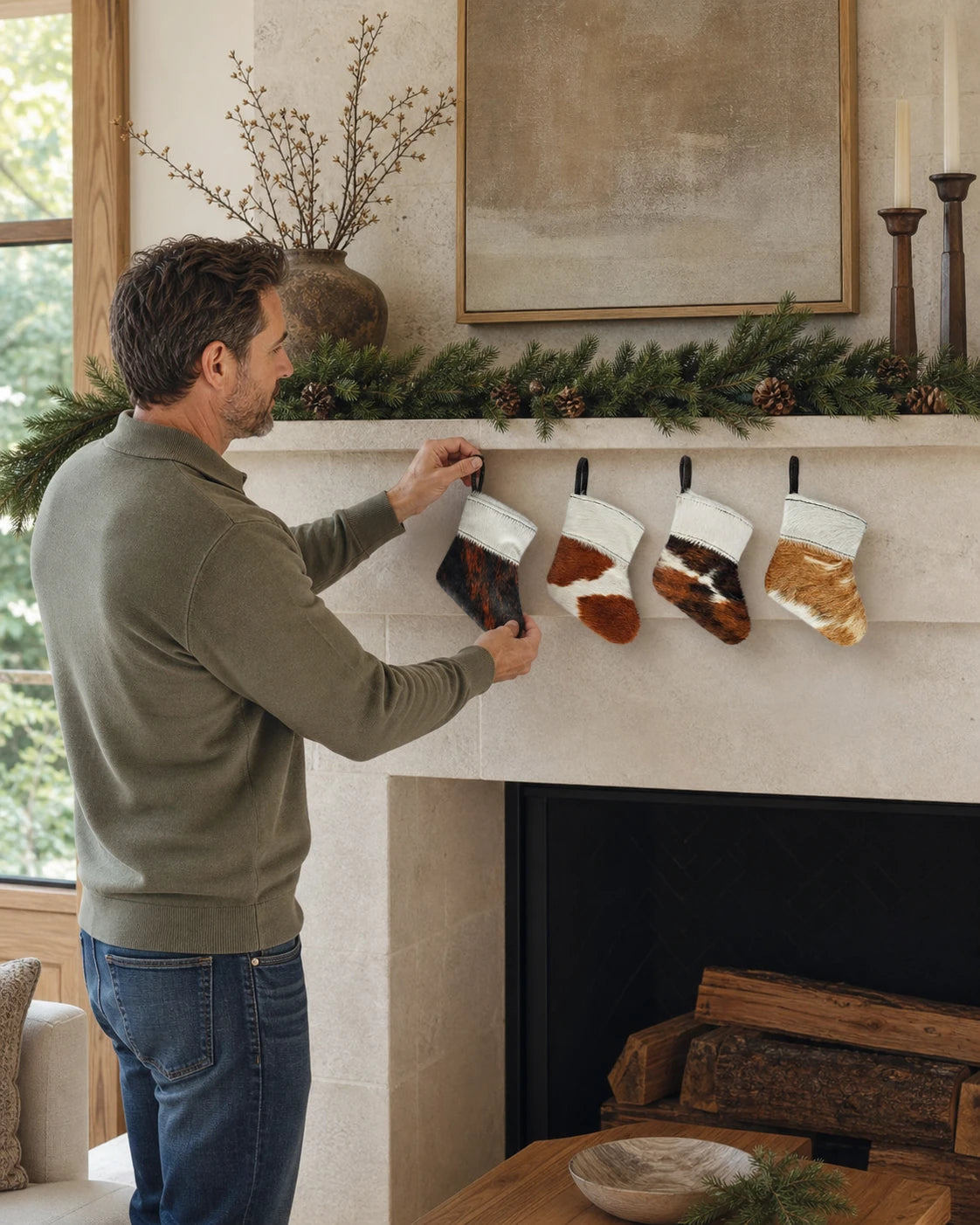 Capricornus Living Four-piece cowhide holiday stocking ornament set being installed on an American fireplace mantel