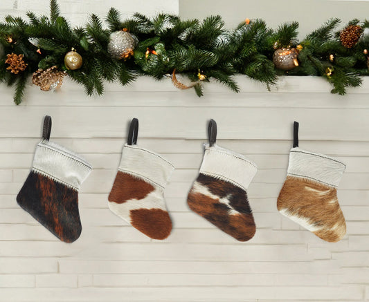 Capricornus Living Four-piece cowhide mini holiday stocking ornament set displayed beneath an evergreen mantel garland