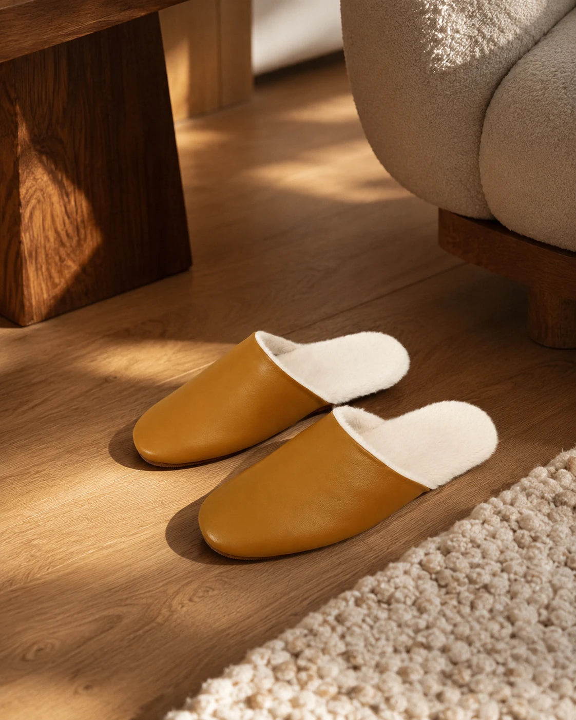 Capricornus Living Cognac lambskin plush-lined slippers arranged on a warm wood floor