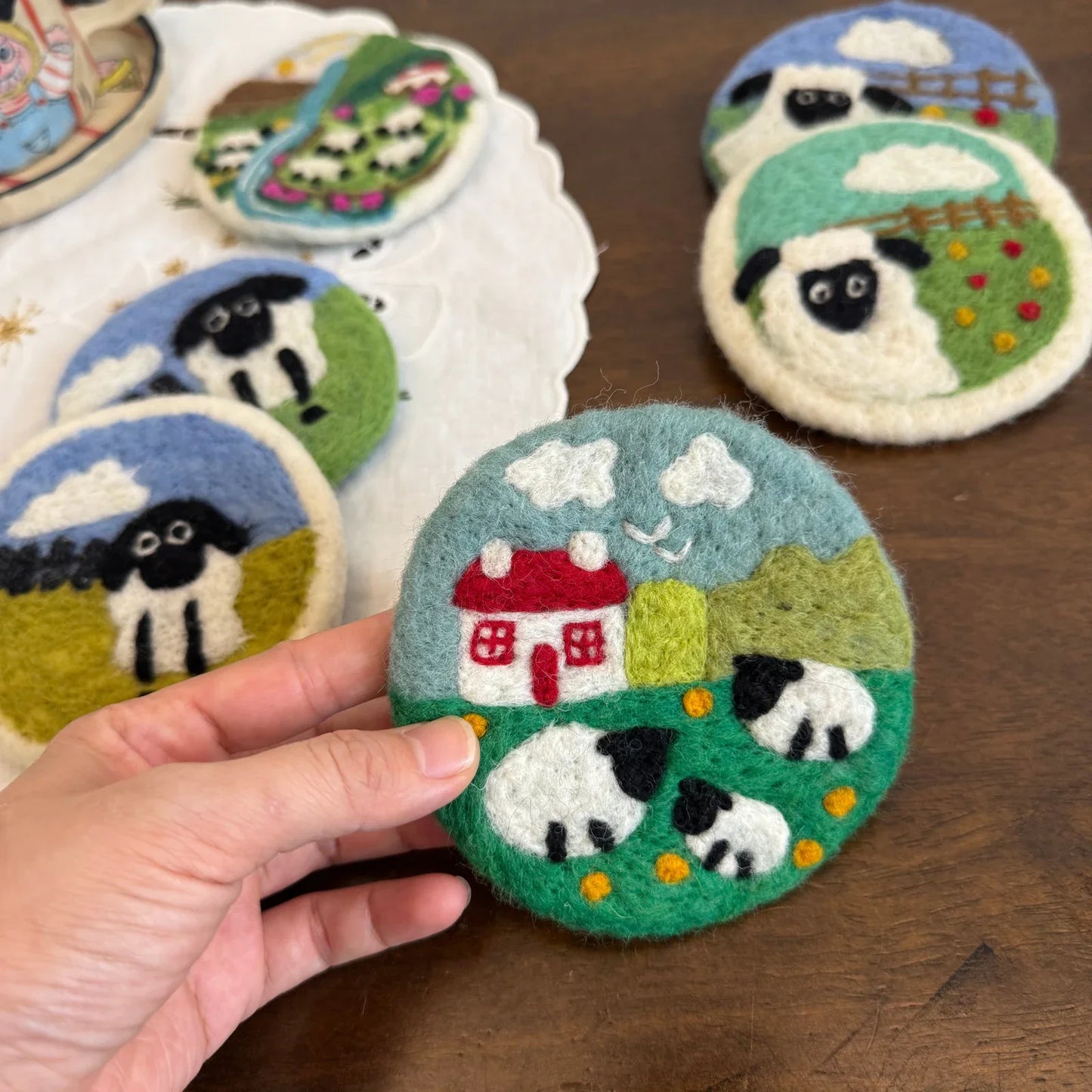 Handmade wool felt pastoral coasters styled on a warm wooden table