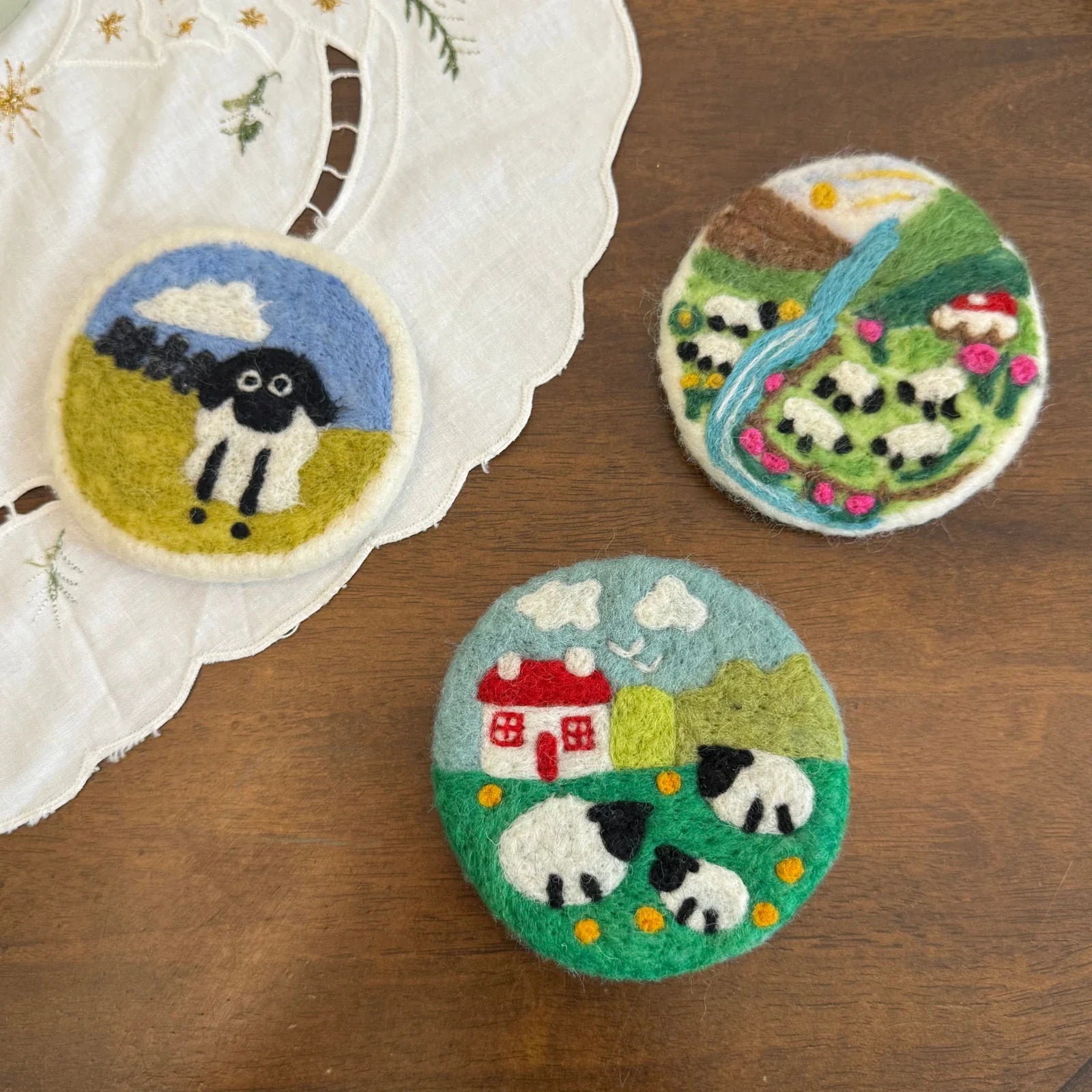 Sheep and countryside wool felt coasters arranged on a natural wood table