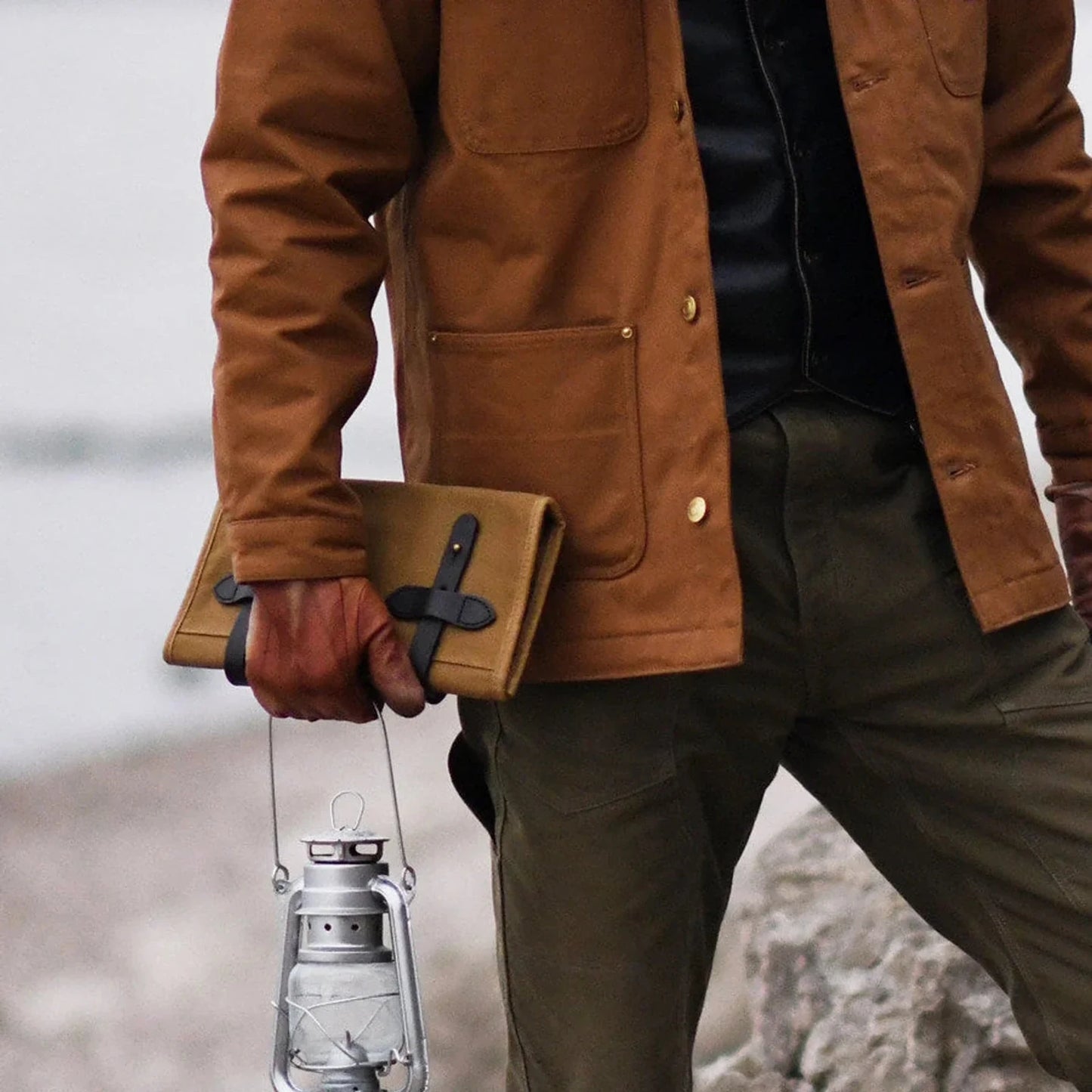 Waxed canvas roll-up tool organizer carried by hand in an outdoor setting