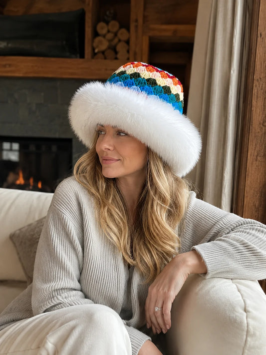 Woman wearing a white fox-fur-trim crochet bucket hat in a fireside cabin