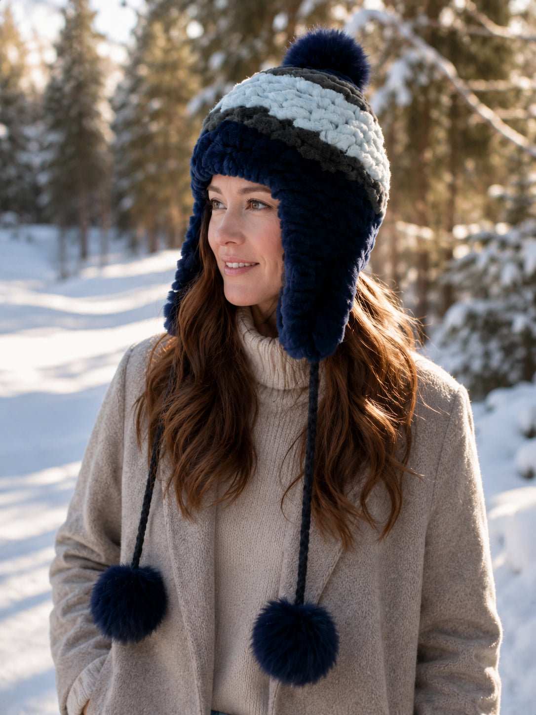 Women's blue Rex rabbit fur earflap hat with fox fur pom-poms in a snowy winter setting