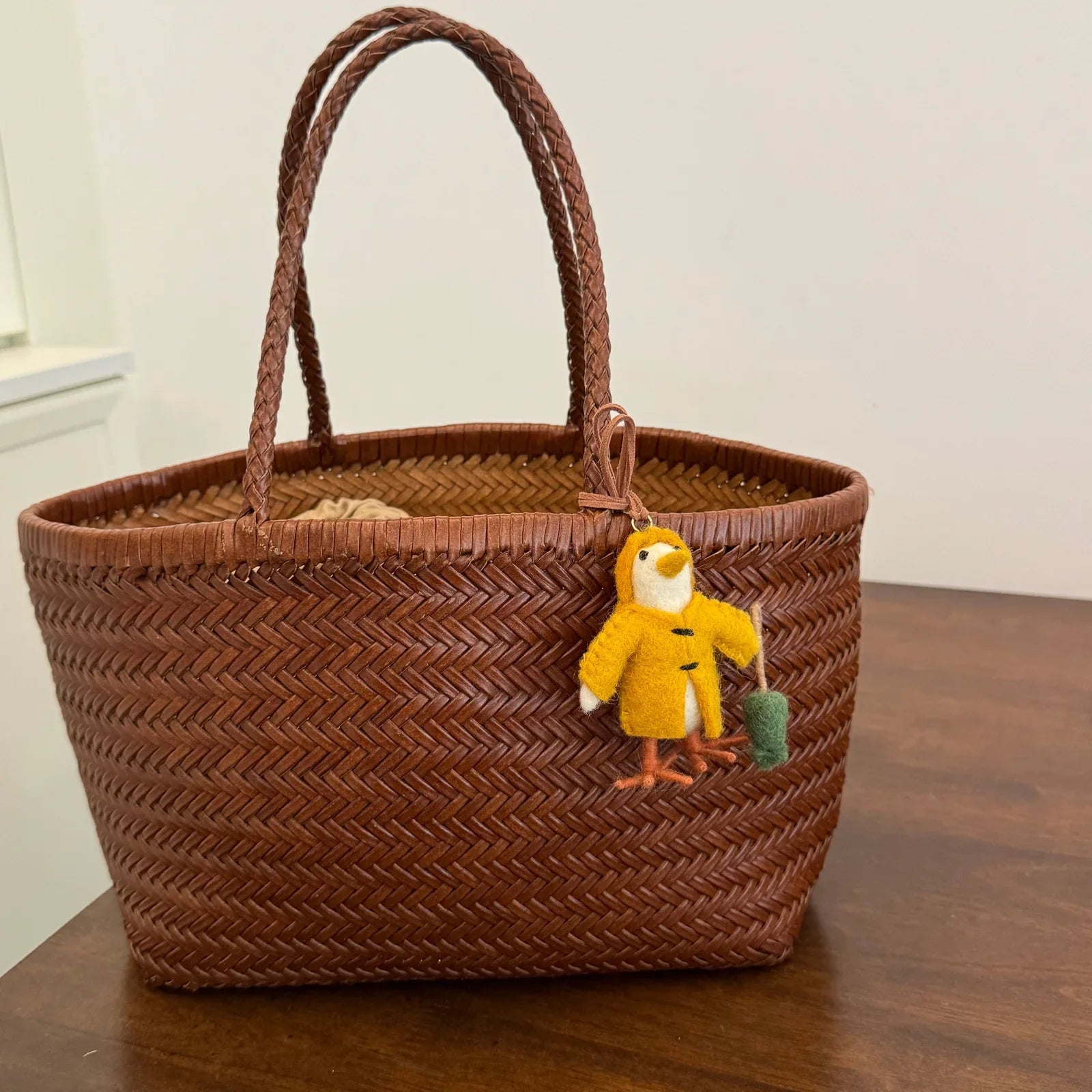 Yellow wool felt chick charm styled on a woven basket bag