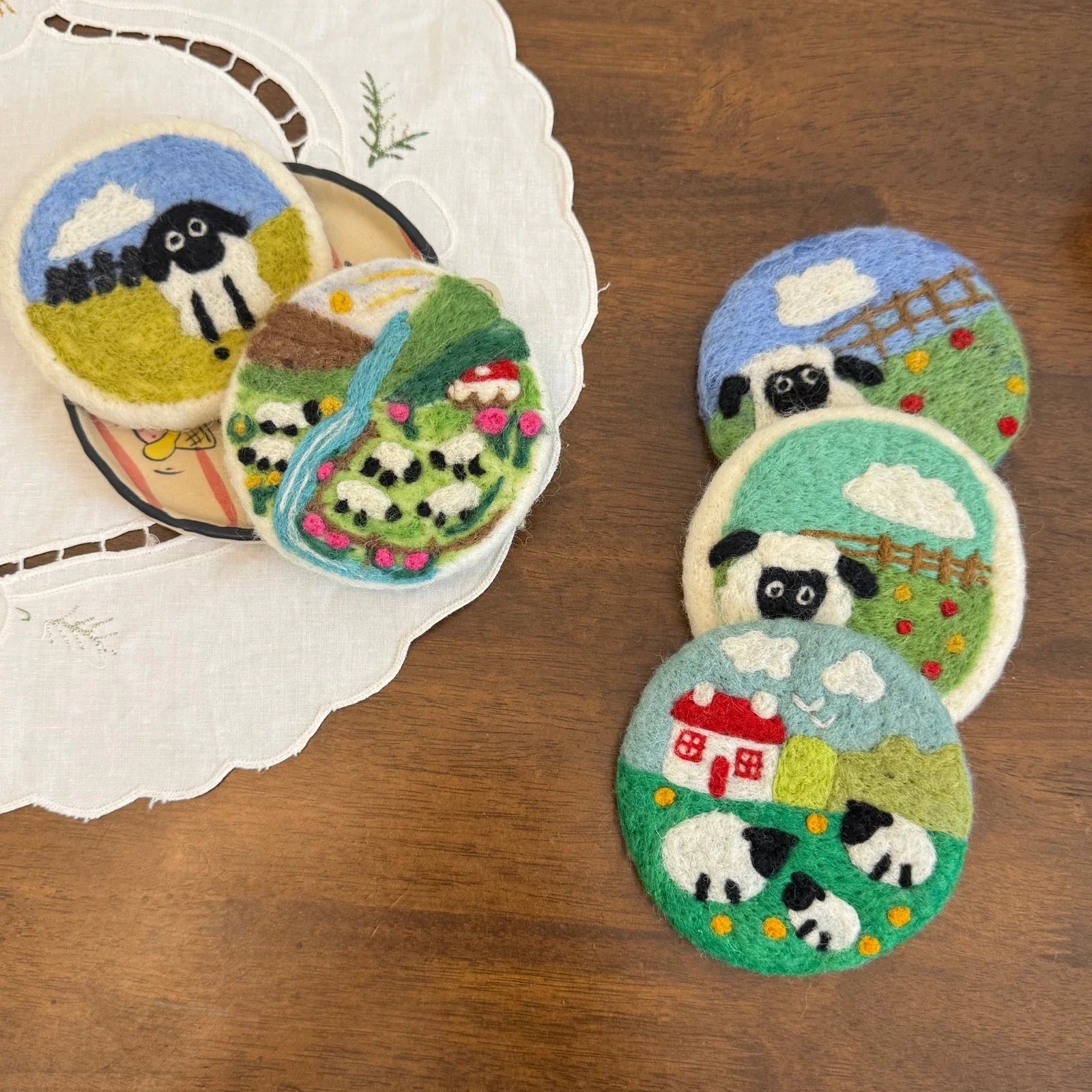 Pastoral wool felt coasters beside embroidered linen on a wooden table