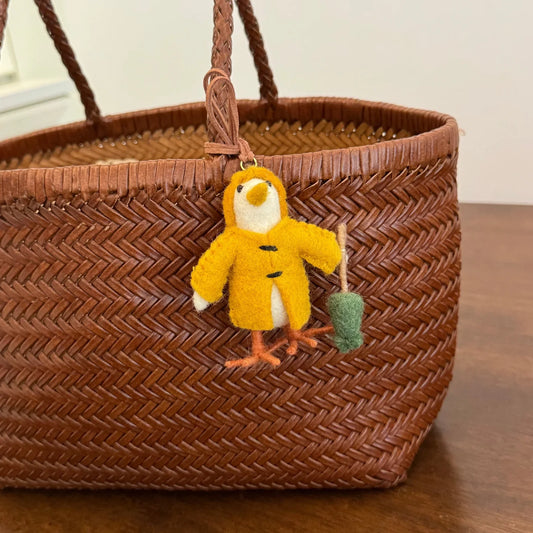 Yellow handmade wool felt chick charm hanging from a woven bag